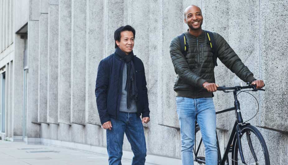 Hombres caminando por la ciudad con bicicleta hablando de economía sanitaria y probióticos